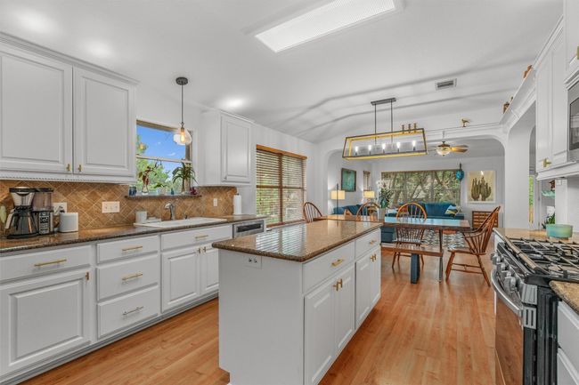 Kitchen with stainless steel appliances, a ceiling fan, backsplash, a center island, and light wood-style flooring | Image 9