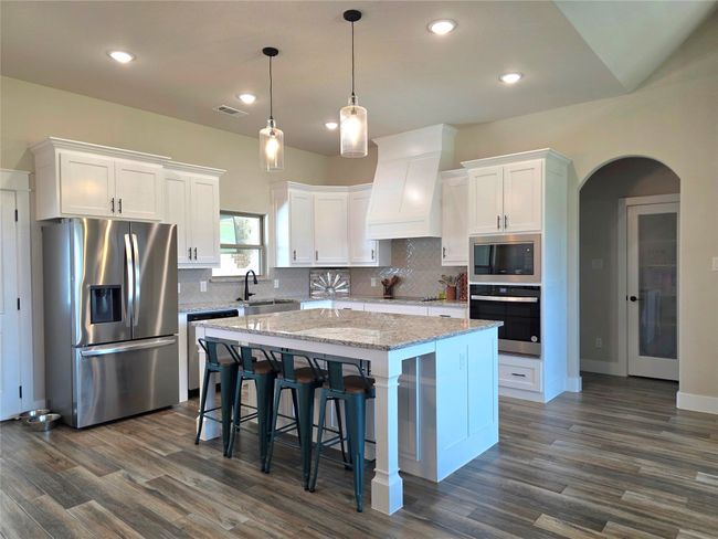 Kitchen with black appliances, a center island, white cabinets, custom range hood, and arched walkways | Image 11