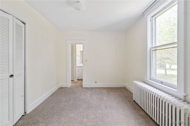 Bedroom with radiator, light colored carpet, baseboards, and a closet | Image 11