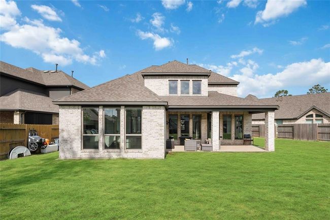 This is a modern two-story home with a spacious backyard, featuring a covered patio perfect for outdoor relaxation. The exterior is composed of light brick and numerous large windows, offering plenty of natural light. | Image 34