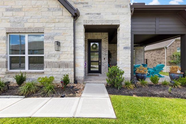 Modern stone with a welcoming front entrance, complete with a glass door and tidy landscaping. A cozy patio area with bright seating offering a perfect spot for relaxation. | Image 11