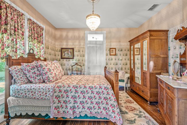 Bedroom with wallpapered walls, visible vents, wood finished floors, and an inviting chandelier | Image 21