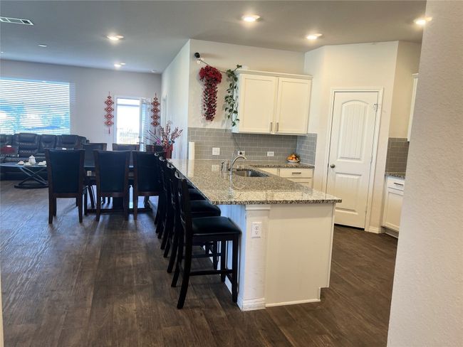 Kitchen with dark wood-style flooring, a kitchen breakfast bar, white cabinets, light stone countertops, and a peninsula | Image 5