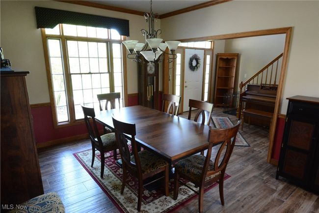 Dining area featuring a chandelier, healthy amount of natural light, crown molding, wood finished floors, and stairway | Image 9