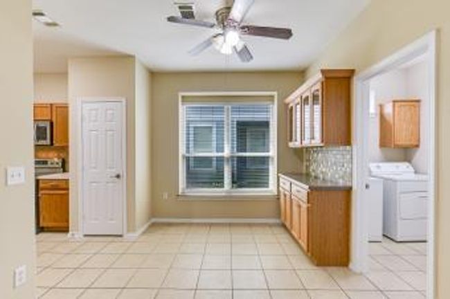Kitchen featuring stainless steel microwave, a ceiling fan, brown cabinets, decorative backsplash, and light tile patterned flooring | Image 4