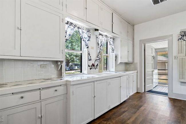Kitchen with light countertops, white cabinets, tasteful backsplash, and wood flooring. | Image 12