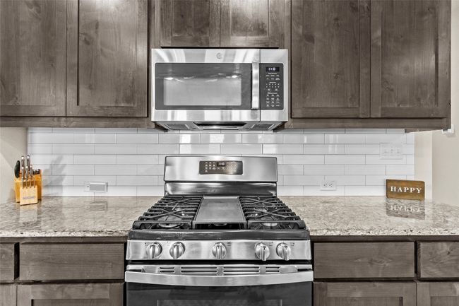 Kitchen with stainless steel appliances, dark brown cabinetry, tasteful backsplash, and light stone countertops | Image 6