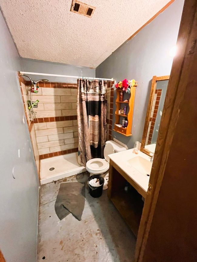 Bathroom with a textured ceiling, unfinished concrete flooring, a stall shower, toilet, and vanity | Image 12
