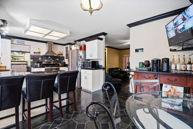 Kitchen featuring dark countertops, crown molding, appliances with stainless steel finishes, wall chimney range hood, and white cabinets | Image 12