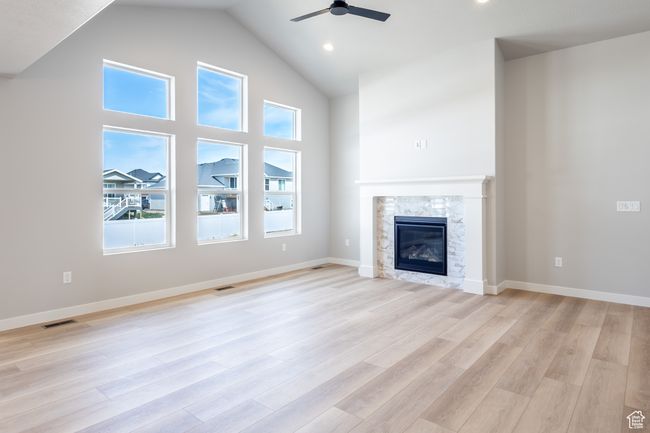 Unfurnished living room with a ceiling fan, plenty of natural light, high vaulted ceiling, a glass covered fireplace, and light wood-style flooring | Image 6