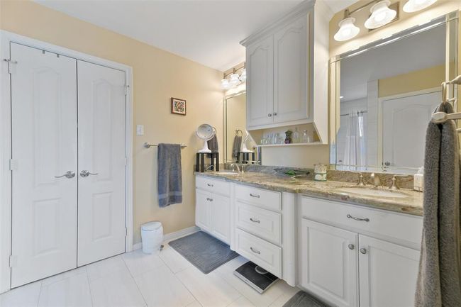 This bathroom features a dual-sink vanity with a granite countertop, ample cabinet storage, and large mirrors. It has a neutral color palette, elegant lighting fixtures, and a clean, modern design. | Image 28