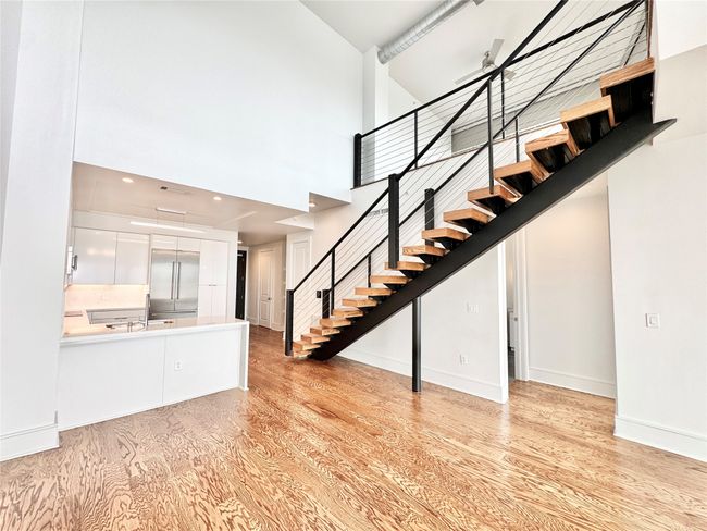 Unfurnished living room featuring stairs, light wood finished floors, a towering ceiling, a sink, and baseboards | Image 6
