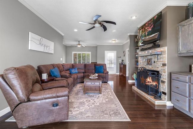 This spacious living room features a cozy stone fireplace, rich hardwood floors, and a plush sectional sofa. Ceiling fans and recessed lighting add comfort and ambiance, while neutral walls enhance the inviting atmosphere. Perfect for relaxation and entertaining. | Image 9