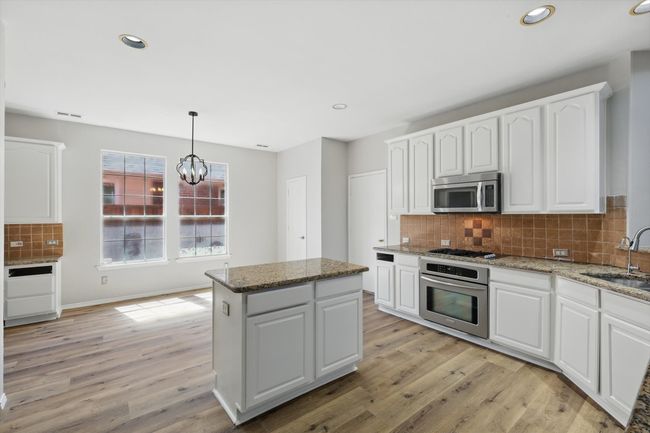 Kitchen with appliances with stainless steel finishes, a sink, a kitchen island, white cabinets, and tasteful backsplash | Image 12