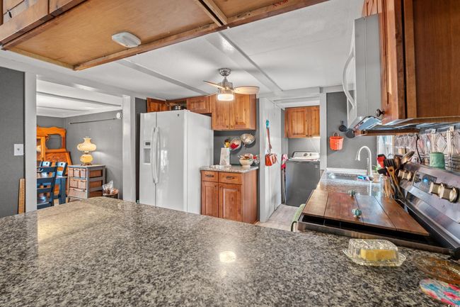 Kitchen featuring ceiling fan, white fridge with ice dispenser, sink, dark stone countertops, and washer / dryer | Image 12