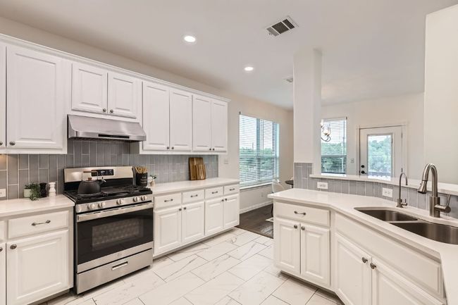 Kitchen with stainless steel gas range oven, under cabinet range hood, a sink, recessed lighting, and light marble finish flooring | Image 8