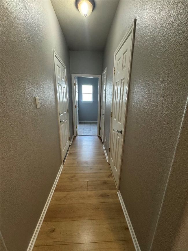 Hall with wood finished floors, baseboards, and a textured wall | Image 11