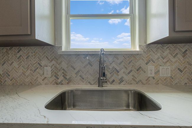This kitchen features a sleek, modern sink with a stainless steel faucet, set in a marble countertop. The stylish herringbone-patterned backsplash adds elegance, while the window above the sink offers natural light and a view. | Image 33