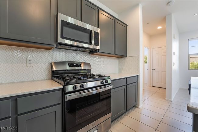 Kitchen featuring appliances with stainless steel finishes, light tile patterned flooring, tasteful backsplash, and light stone counters | Image 17