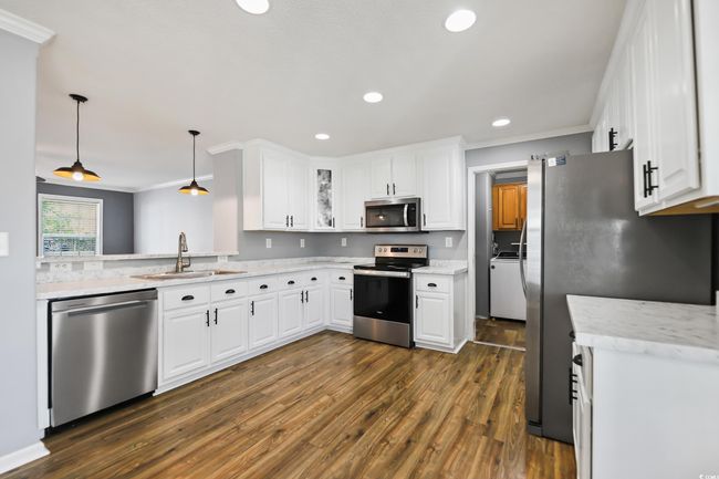 Kitchen with stainless steel appliances, a sink, ornamental molding, dark wood-type flooring, and white cabinets | Image 10