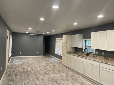 Kitchen featuring light hardwood / wood-style floors, sink, ceiling fan, light stone counters, and white cabinets | Image 2