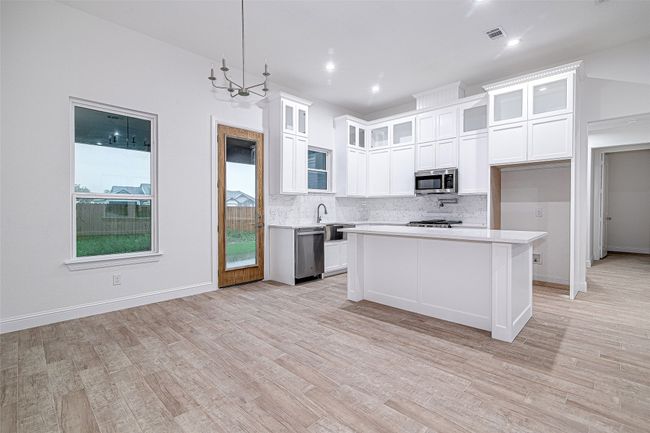 Kitchen with stainless steel appliances, light countertops, backsplash, light wood-style floors, and white cabinets | Image 10