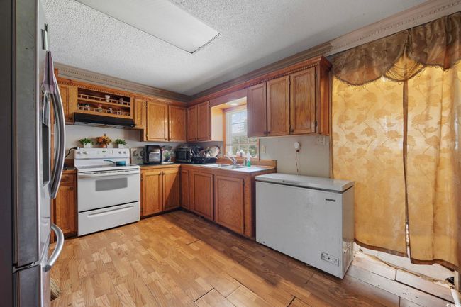 Kitchen featuring white electric range oven, stainless steel refrigerator with ice dispenser, refrigerator, a textured ceiling, and light wood-style floors | Image 9