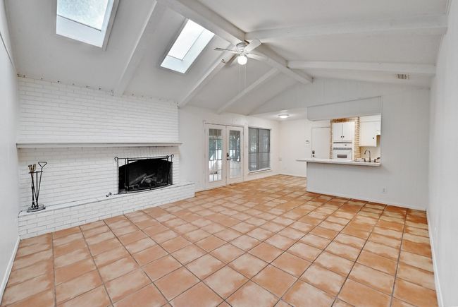 Unfurnished living room featuring vaulted ceiling with skylight, a ceiling fan, visible vents, a sink, and a brick fireplace | Image 4