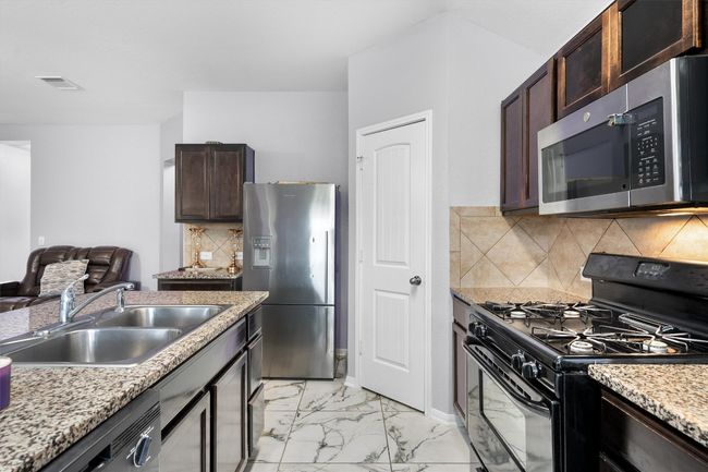 Kitchen featuring appliances with stainless steel finishes, a sink, light marble finish floors, dark brown cabinetry, and decorative backsplash | Image 9