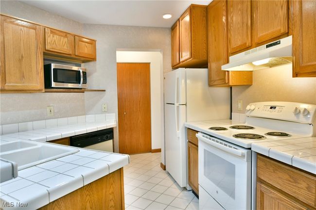 Kitchen featuring white appliances, under cabinet range hood, tile countertops, and light tile patterned floors | Image 11