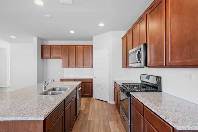 Kitchen with stainless steel appliances, tasteful backsplash, light wood-style floors, light stone counters, and brown cabinetry | Image 10