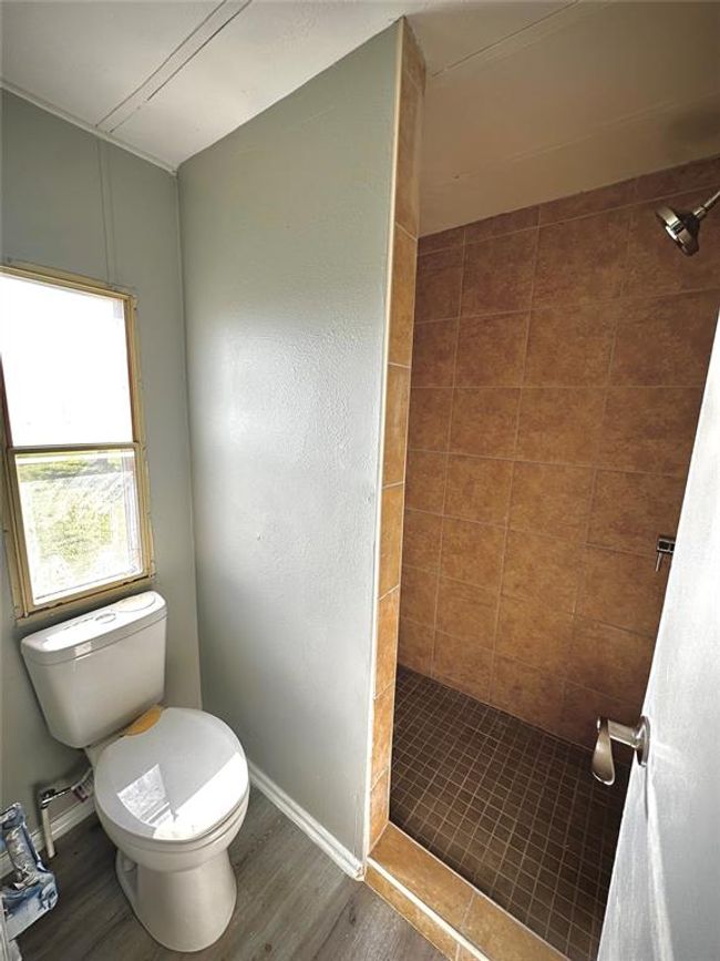 Full bath featuring a shower stall, toilet, wood finished floors, and baseboards | Image 9