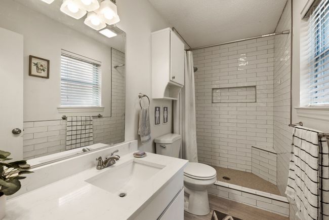 Full bathroom featuring a textured ceiling, toilet, a tile shower, wood finished floors, and vanity | Image 16