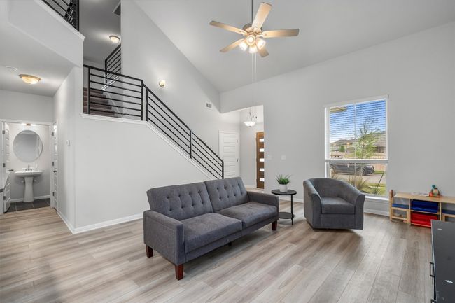 Living area featuring light wood finished floors, stairs, a towering ceiling, ceiling fan, and baseboards | Image 5