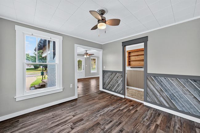 Unfurnished room featuring plenty of natural light, dark wood finished floors, a wainscoted wall, crown molding, and ceiling fan | Image 7