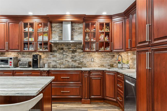 Kitchen with sink, dishwasher, light stone counters, decorative backsplash, and wall chimney exhaust hood | Image 5