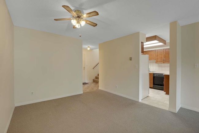 Unfurnished living room featuring light carpet, a ceiling fan, and stairs | Image 10