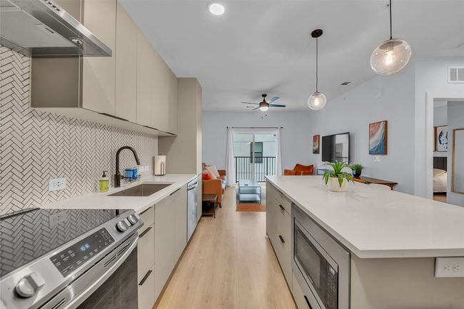 Kitchen featuring stainless steel appliances, modern cabinets, under cabinet range hood, and decorative backsplash | Image 14