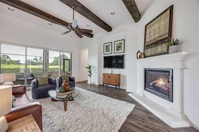Living room with a glass covered fireplace, dark wood-type flooring, beam ceiling, a ceiling fan, and recessed lighting | Image 5