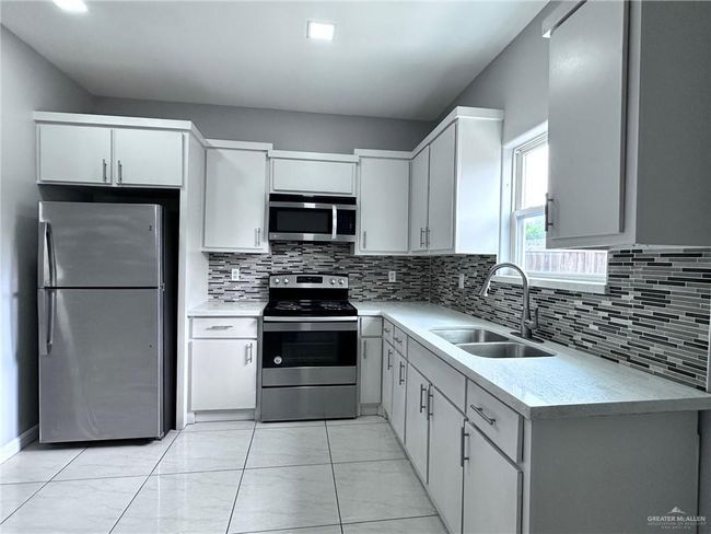 Kitchen with light countertops, decorative backsplash, a sink, white cabinets, and appliances with stainless steel finishes | Image 8