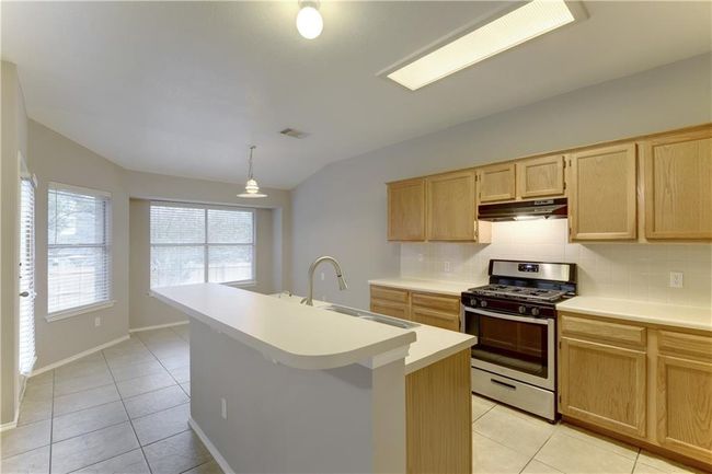 Kitchen with gas range, white dishwasher, backsplash, light tile patterned floors, and light countertops | Image 6