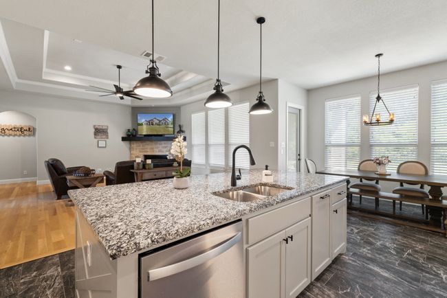 Kitchen with stainless steel dishwasher, a sink, a center island with sink, a fireplace, and white cabinetry | Image 12