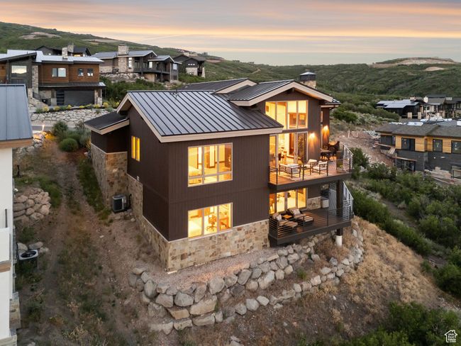 Rear view of house featuring stone siding, a standing seam roof, a chimney, a metal roof, and a balcony | Image 62