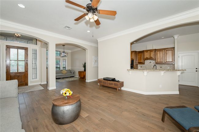 Living room with arched walkways, wood finished floors, baseboards, a ceiling fan, and crown molding | Image 5