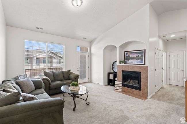 Living room with baseboards, a tile fireplace, light carpet, and lofted ceiling | Image 6