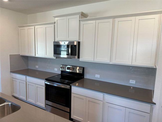 Kitchen featuring dark countertops, decorative backsplash, stainless steel appliances, and white cabinets | Image 10