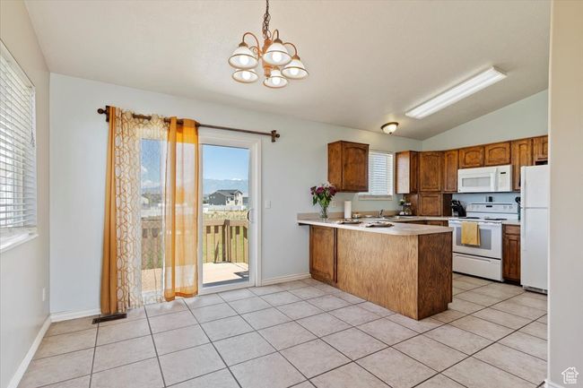 Kitchen with white appliances, a peninsula, a chandelier, vaulted ceiling, and light countertops | Image 8
