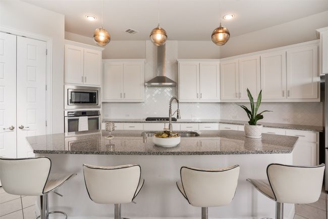 Kitchen with stainless steel appliances, a breakfast bar, wall chimney range hood, visible vents, and white cabinetry | Image 10