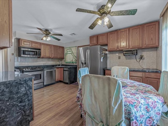 Kitchen featuring appliances with stainless steel finishes, a ceiling fan, backsplash, and brown cabinetry | Image 9
