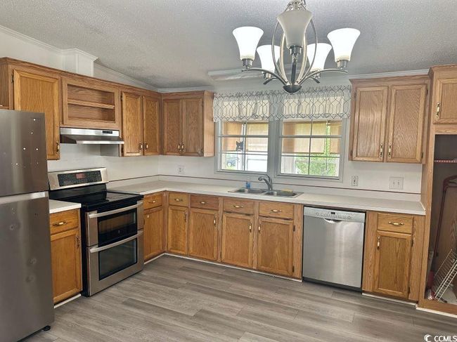 Kitchen featuring appliances with stainless steel finishes, under cabinet range hood, a sink, a textured ceiling, and light countertops | Image 10